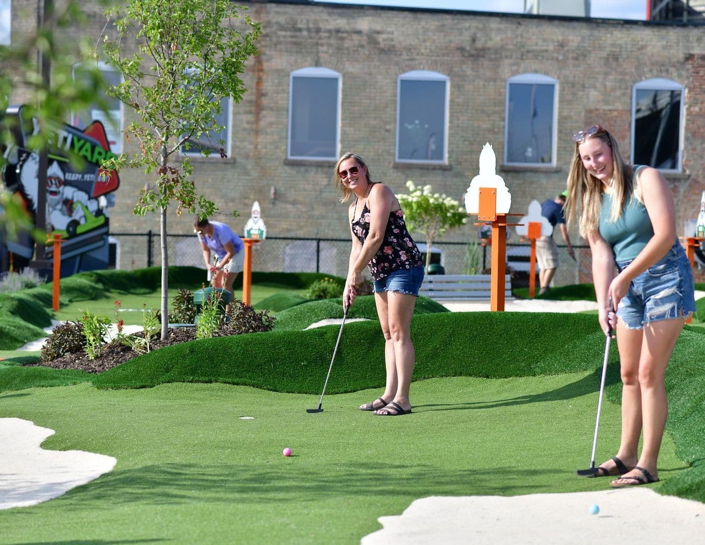 Women playing mini golf on the YetiYard course surrounded by lush landscaping