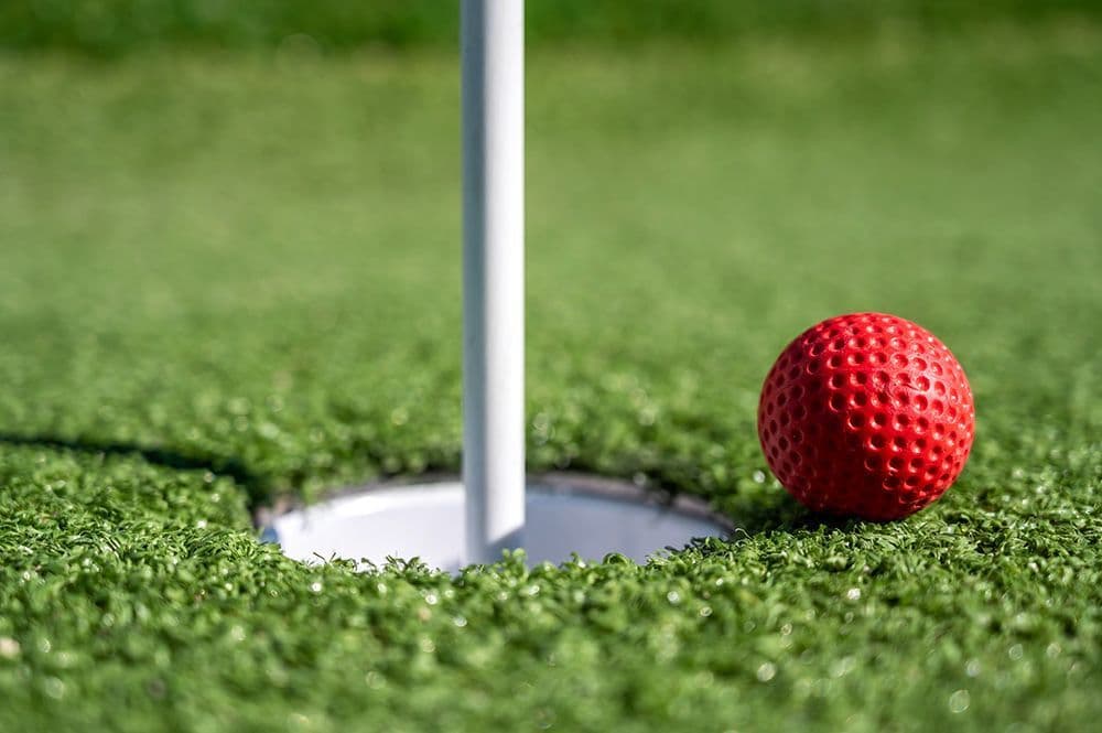 Close-up of a red mini golf ball near the hole on real turf at YetiYard